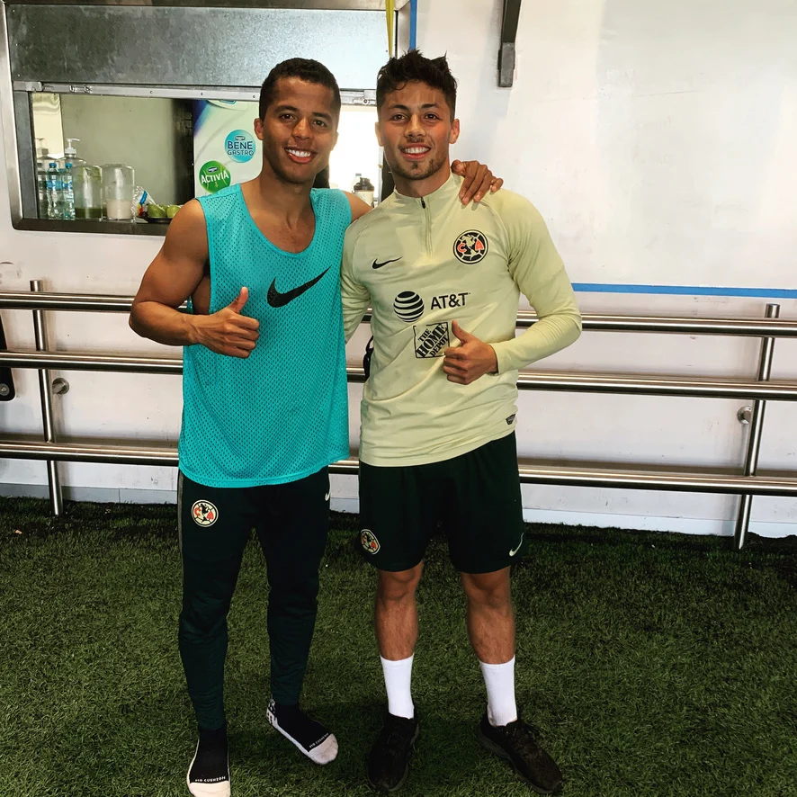 Adrian Goransch in a Club America training top beside Giovanni dos Santos, both smiling with thumbs up